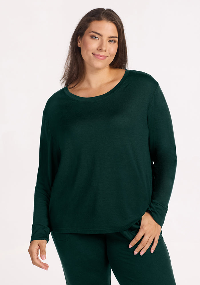 A smiling woman wears an Ashlie Lounge Top in Deep Pine, a long-sleeved, wrinkle-resistant merino wool lounge top. 