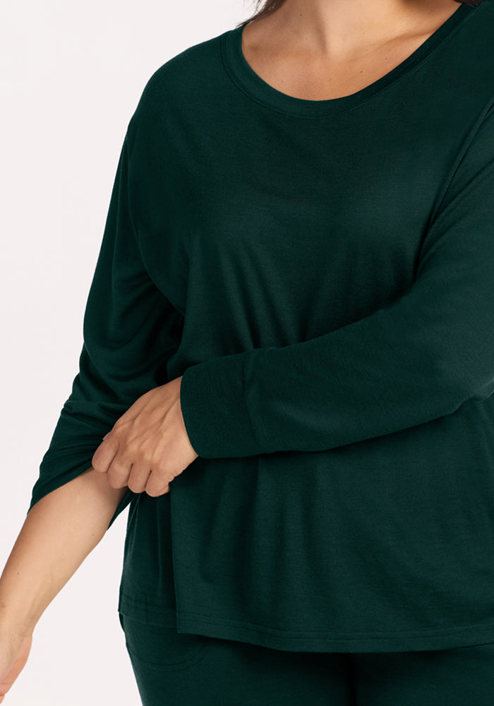 A person wears a dark green Ashlie Lounge Top in Deep Pine, a long-sleeved merino wool top with a round neckline.