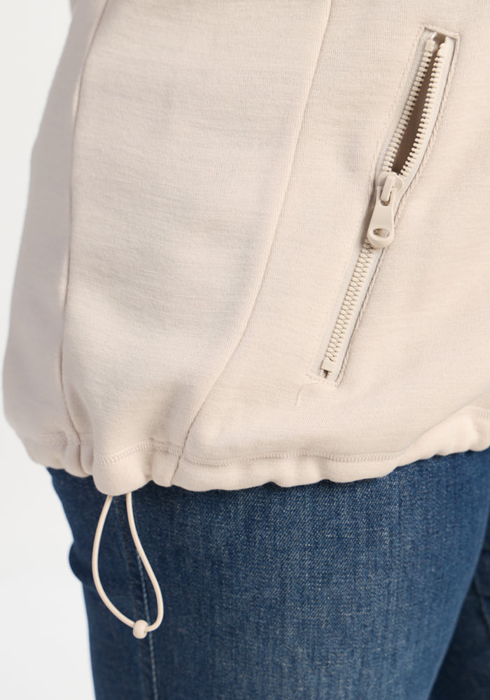 Ecru Teddy Sweatshirt in ultra-heavyweight merino wool with a zippered pocket and drawstring hem over blue jeans.