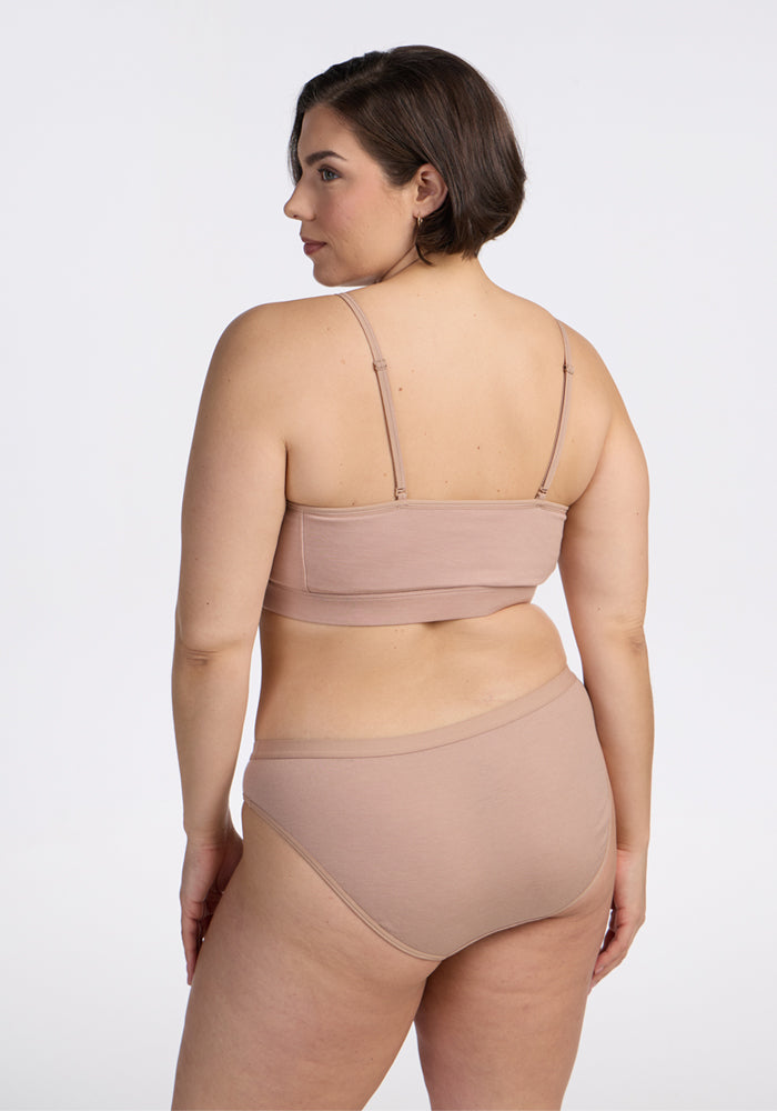 A woman with short brown hair, seen from behind, wears a light beige bralette and Woolx Roxie Bikini Underwear in Morning Latte, set against a plain white background.