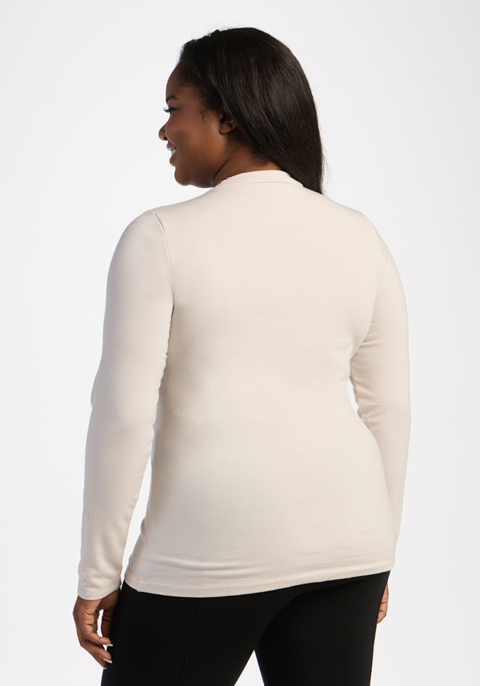 Woman in Woolx Sadie Baselayer Top - Ecru and black pants, shown from the back, smiling over her shoulder.