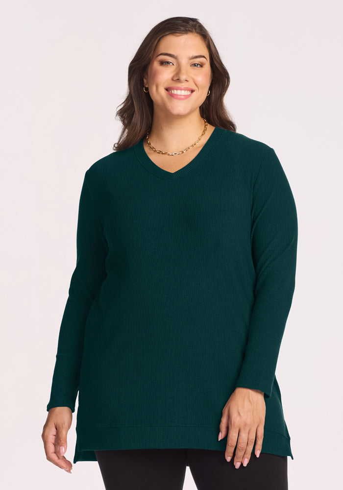 Woman in Woolx Evie Ribbed Tunic - Deep Pine, smiling and styled chic with long brown hair and black pants. 