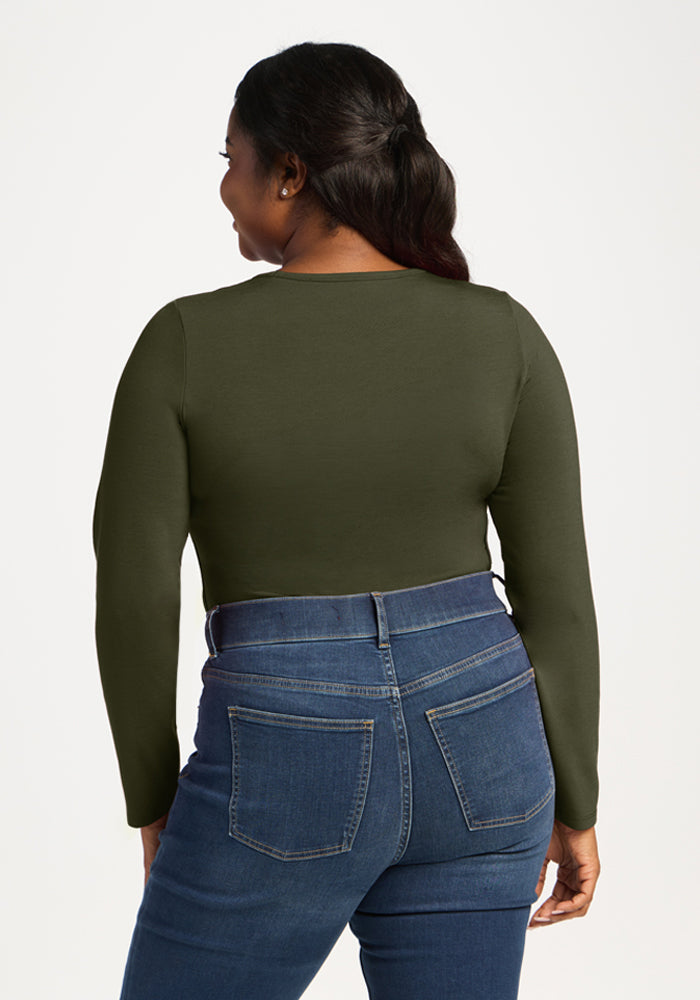 Woman with long dark hair wears Woolx Margot Bodysuit - Everleaf, green top, and blue jeans, shown from the back.