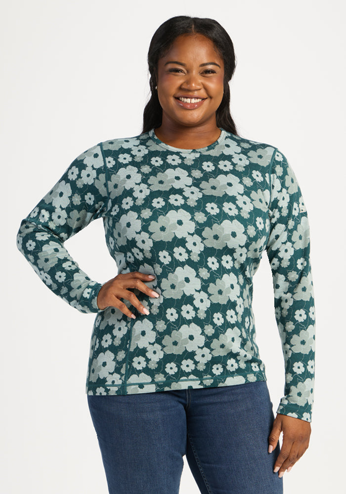 Smiling woman in Woolx Maddie Baselayer Top - Coastal Wildflower and blue jeans, posed against a plain white background. 