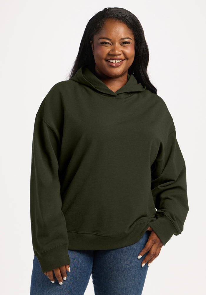 A woman wearing a dark olive green Woolx Genevieve Hoodie - Duffel Bag and blue jeans. 