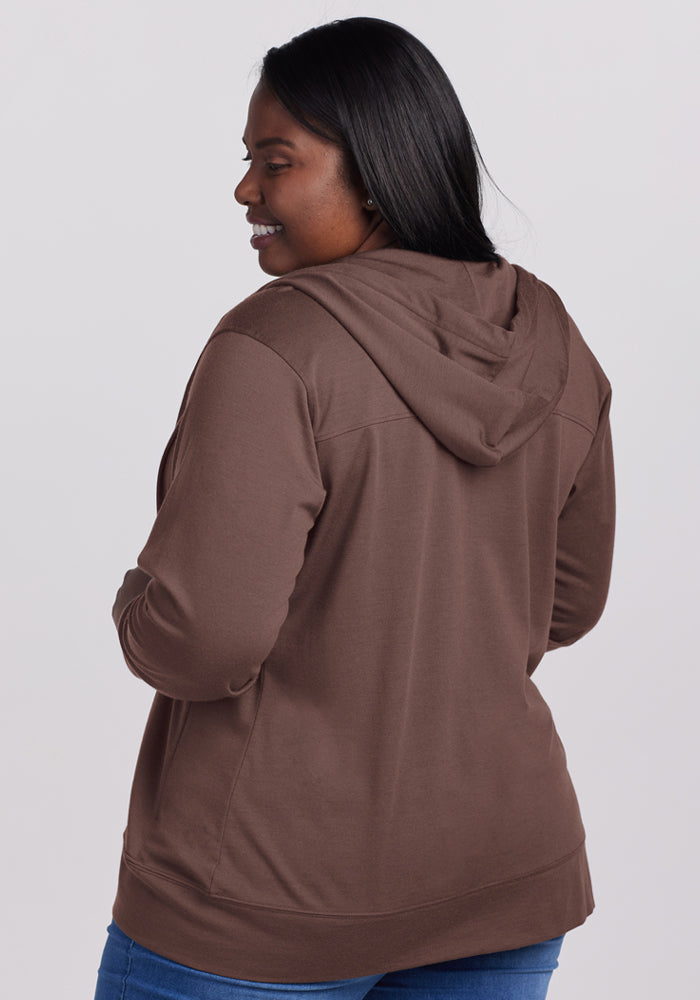 A woman with long dark hair smiles, facing away in a Woolx Ryann Hoodie - Peppercorn and blue jeans.