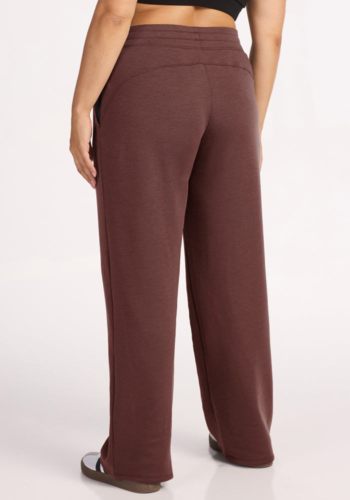 Model wears Woolx Bree Lounge Pants in Canyon Clay with sandals, back view, against a white background.