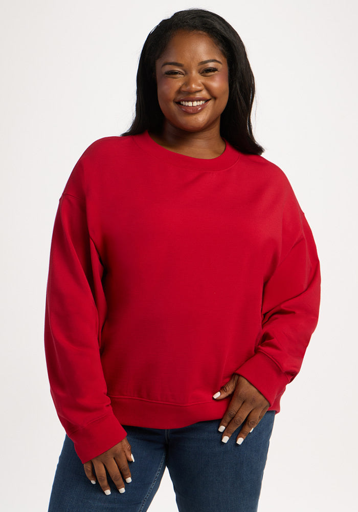 A smiling woman wears a red Woolx Molly Crewneck - Maraschino Cherry moisture-wicking long-sleeved sweatshirt. 