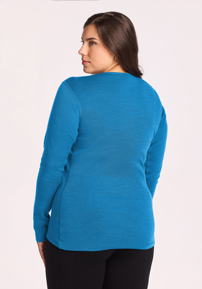 A woman with long brown hair wears the Woolx Hannah Long Sleeve Top - Blue Razz, facing away from the camera.