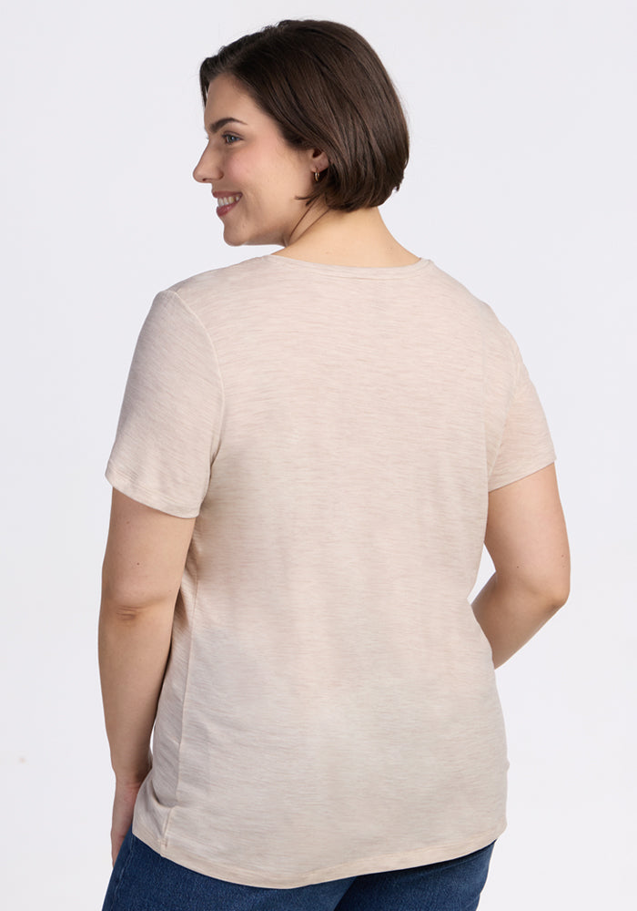 A woman with short brown hair stands smiling, back to the camera, wearing the Woolx Junie V Neck in Cream Heather and blue jeans against a plain white background.