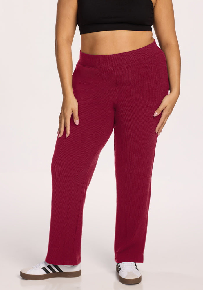 Person in a black crop top, Woolx Luca Ribbed Pants - Beet Red, and white sneakers stands against a white background. 