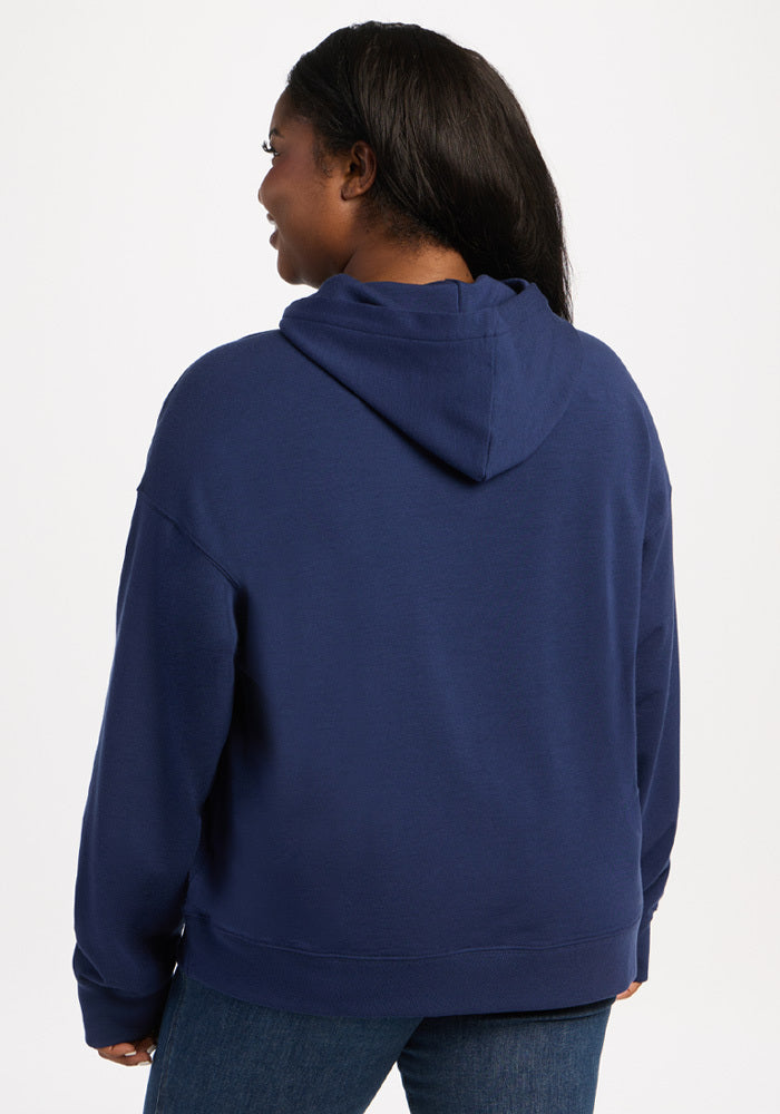 A person seen from behind wearing an Ocean Cavern Genevieve Hoodie made of dark blue moisture-wicking merino wool.
