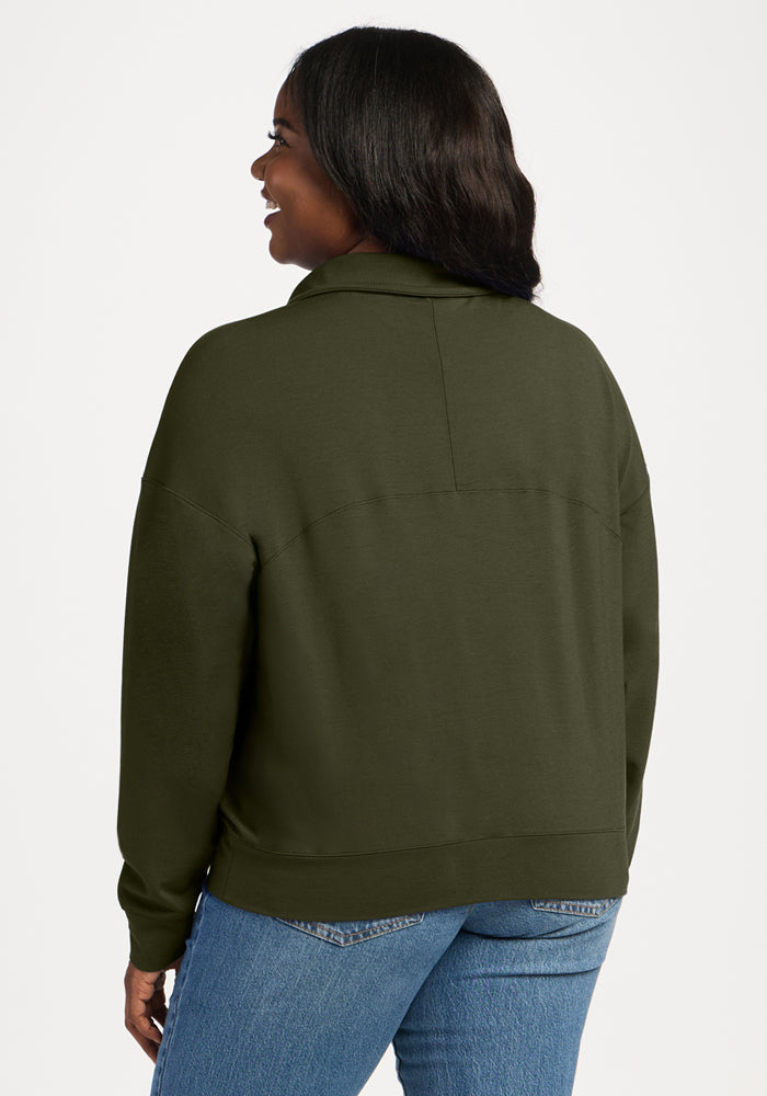 Back view of a woman wearing a dark olive green Woolx Tori 1/4 Zip - Everleaf and blue jeans.