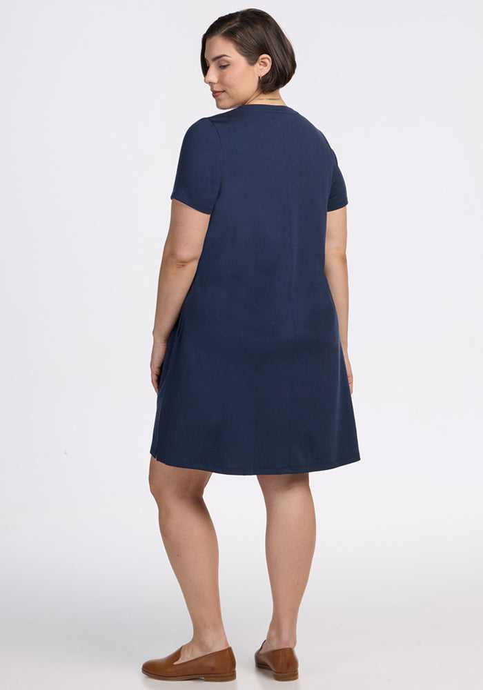 A woman with short brown hair stands facing away from the camera in a knee-length, short-sleeved Woolx Georgie Dress in Deep Navy and brown loafers against a plain white background.