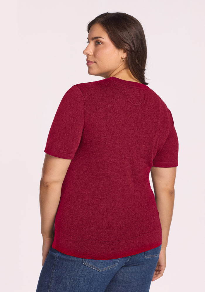 Woman in the Woolx Anna Crew Sweater - Beet Red and blue jeans stands back to camera, glancing over her shoulder.