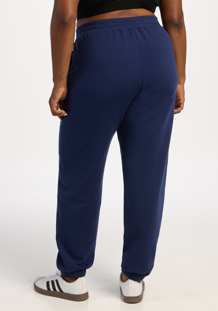 Person in Woolx Parker Sweatpants - Ocean Cavern, white sneakers, black top; back view, plain background.