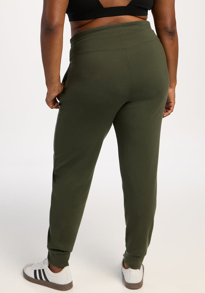 Person wears Woolx Madden Joggers - Everleaf, black top, white sneakers; stands against a plain background.