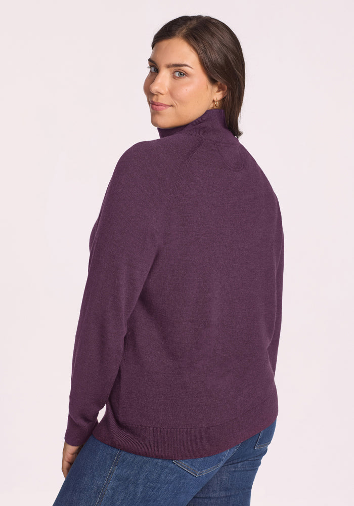 Woman in Woolx Collins Half Zip Sweater - Purple Iris and jeans looks over her shoulder, turned slightly from camera.