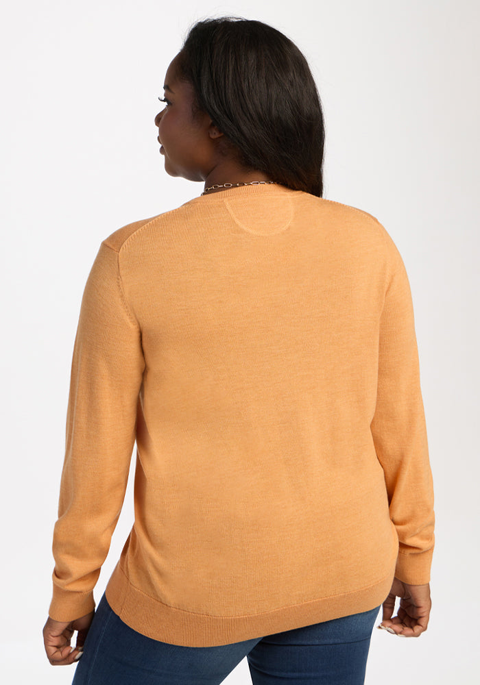 Someone wearing the Woolx Francesca Sweater in Butterscotch and blue jeans stands with their back to a white backdrop.