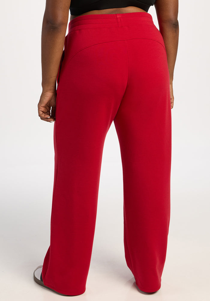 Person in Woolx Bree Lounge Pants - Maraschino Cherry, relaxed fit, wide-leg, with sandals, back view on white.