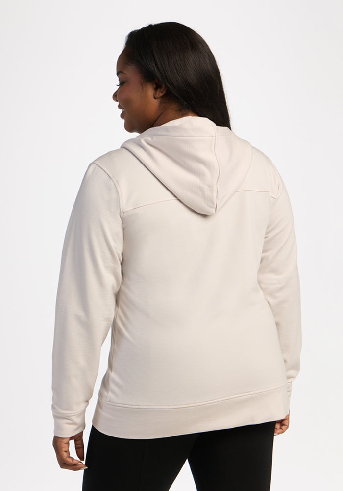 Woman wearing Woolx Darby Zip Up Hoodie in Ecru, facing away, against plain white background.