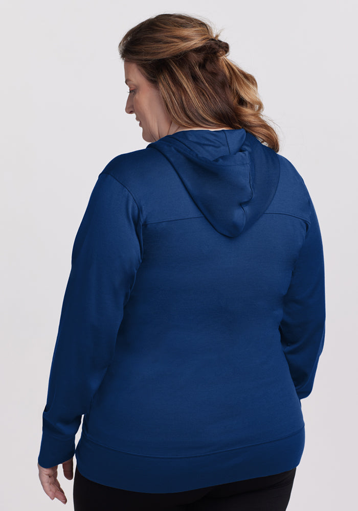 A woman with light brown wavy hair is shown from the back wearing the Woolx Ryann Hoodie in Estate Blue and black pants against a plain light background.