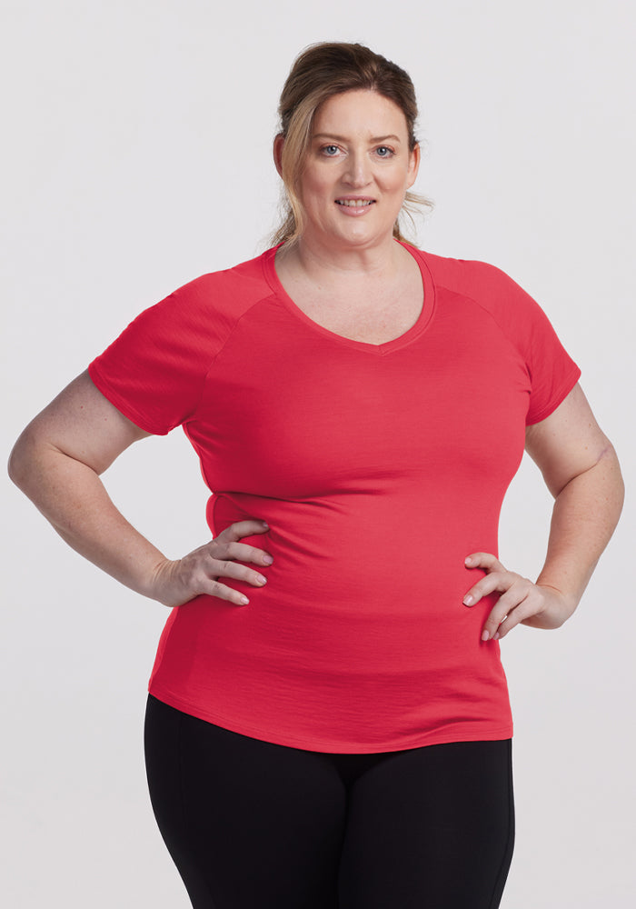 Woman with light brown hair in a ponytail wears Woolx Mia V Neck - Berry Ice Pop, black pants, stands smiling. 