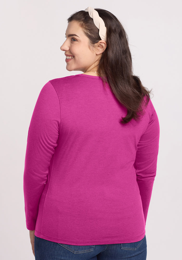 A woman in the Woolx Remi Long Sleeve T-Shirt in Summer Sorbet smiles over her shoulder, hair held back by a headband.