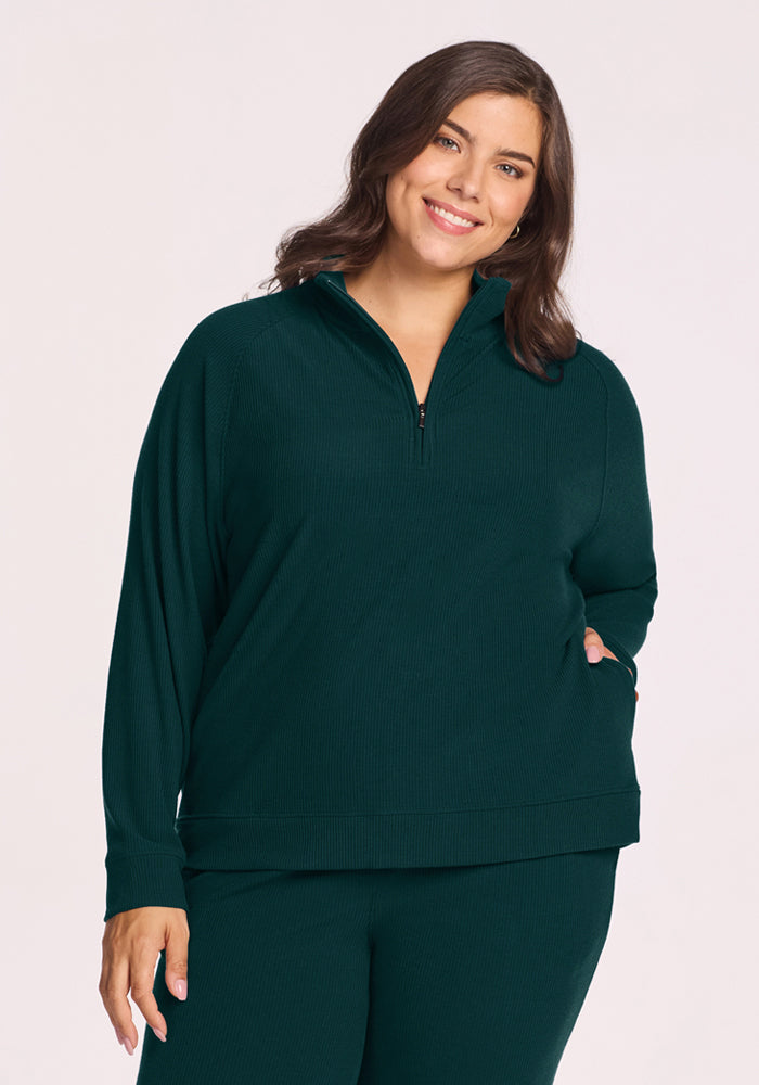 Woman in Woolx Quinn Ribbed 1/4 Zip - Deep Pine, smiling with a hand in pocket against plain background. 