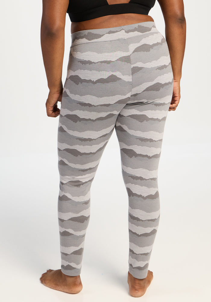 Barefoot person faces away, wearing Woolx Taylor Baselayer Leggings - High Peaks, against a plain backdrop.