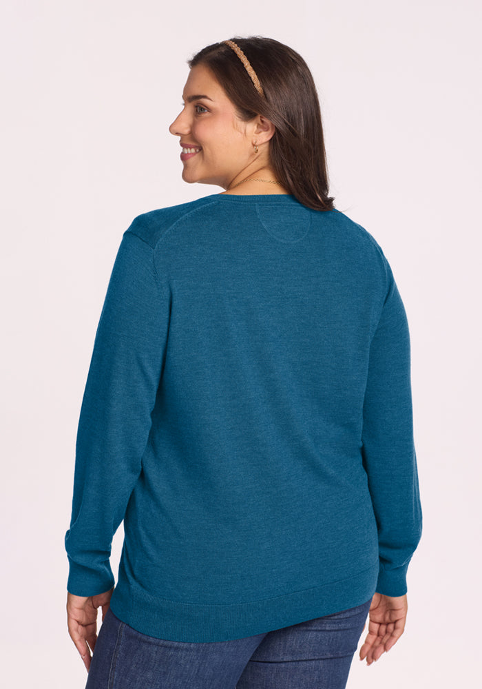 Woman in the Woolx Francesca Sweater - Blue Pine, smiling and glancing back against a light background.