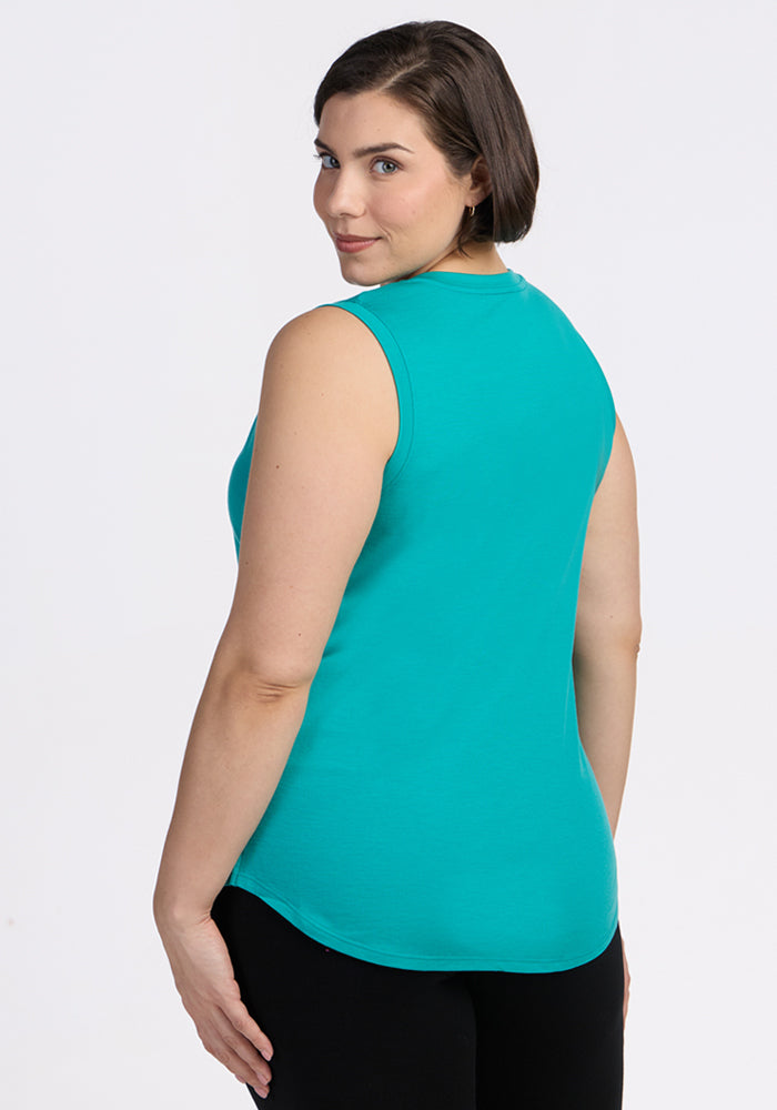A woman with short brown hair wears the Woolx Bella Tunic Top in Cool Jade and black pants, standing slightly turned to the side while looking over her shoulder at the camera against a plain white background.