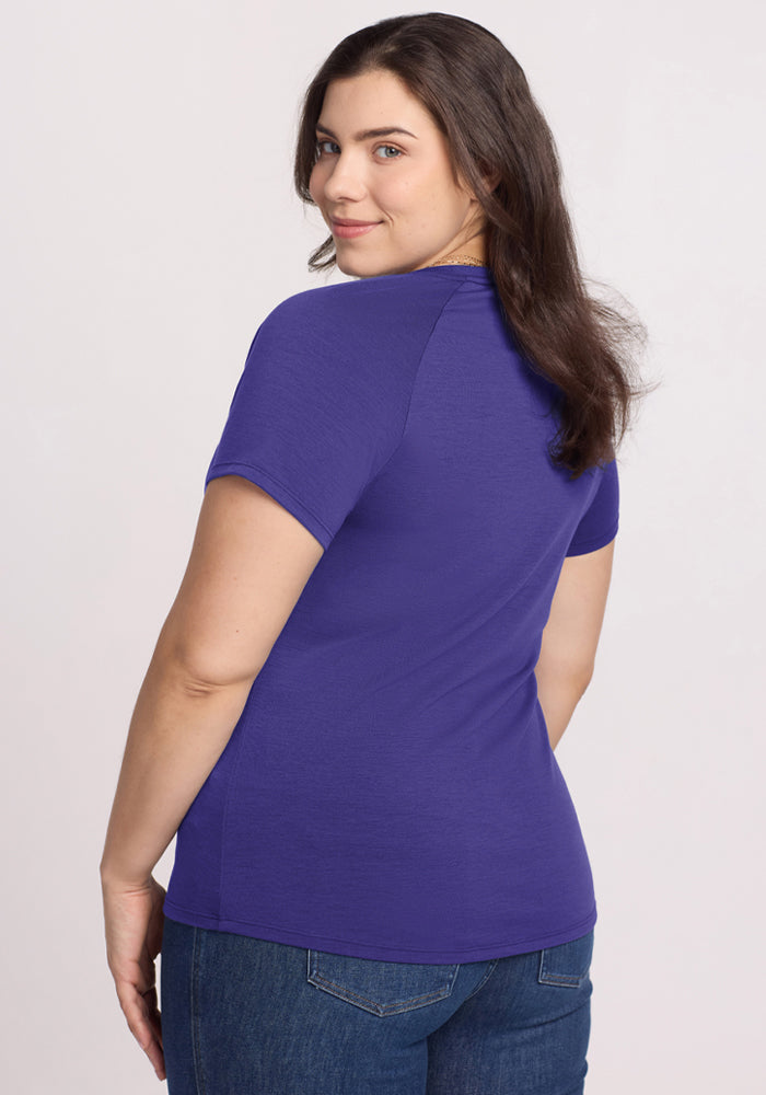 Woman with dark hair in a Woolx Mia V Neck - Berry Indigo tee and blue jeans, smiling over her shoulder at the camera.