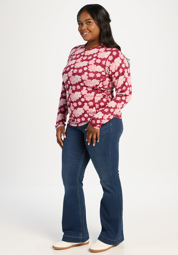 Woman in Woolx Maddie Baselayer Top - Floral Crush, blue jeans, and white shoes, smiling against a white background.