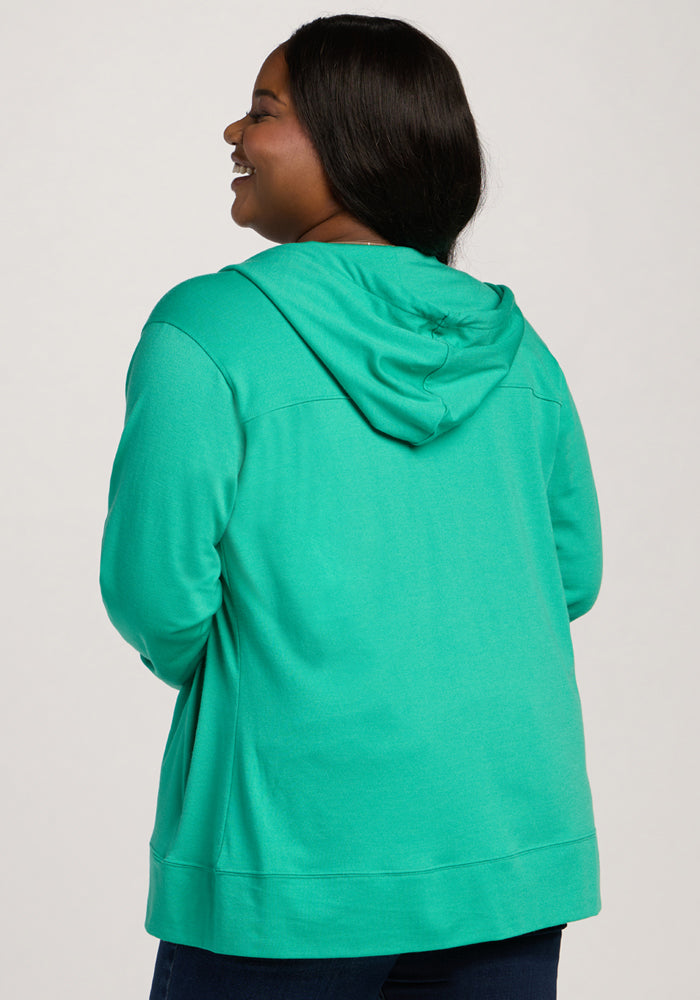Woman smiling and facing away, wearing the Woolx Ryann Hoodie - Jungle and dark pants against a light background.