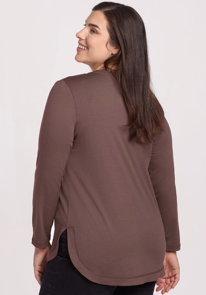 Woman with long brown hair smiles over her shoulder, wearing the Woolx Hazel Tunic in Peppercorn, seen from the back.