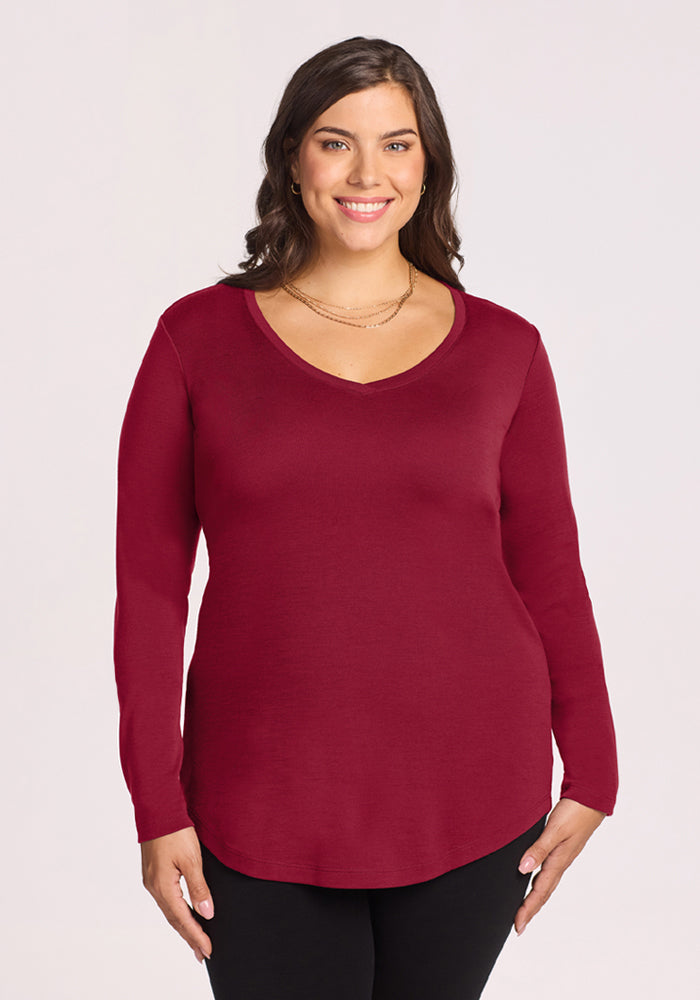 Woman smiling in the Woolx Eva Tunic in Beet Red, a winter must-have, paired with black pants against a light background. 