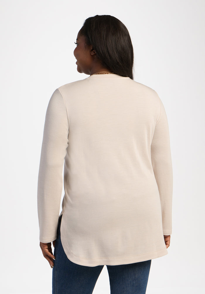 Woman wearing the Woolx Blair Tunic in Ecru and blue jeans, back to camera, standing against a white background.