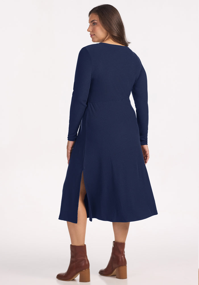 Woman in a Woolx Caroline Ribbed Twirl Dress - Ocean Cavern, standing with her back to the camera in brown boots.