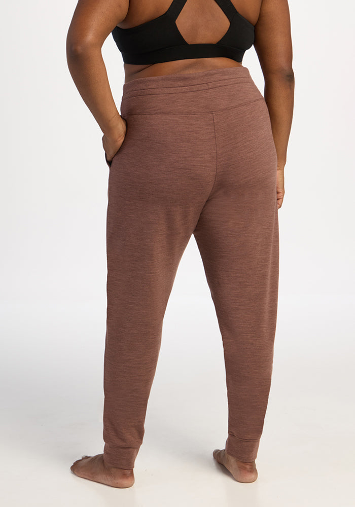 A person in Woolx Willa Joggers Petite - Sable Heather stands barefoot facing away against a white background.