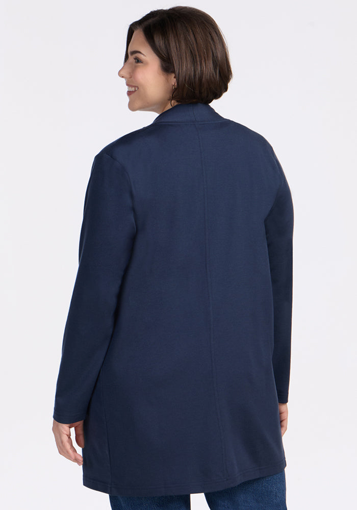 A woman with short brown hair smiles over her shoulder while wearing the Woolx Paisley Cardigan in Deep Navy and blue jeans, facing away against a plain white background.