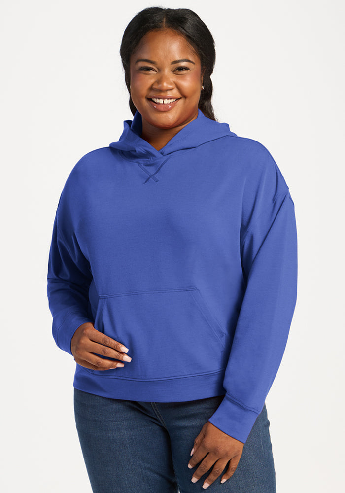 Woman smiling in the Woolx Lizzy Hoodie - Royal Blue and jeans, standing against a plain white background.