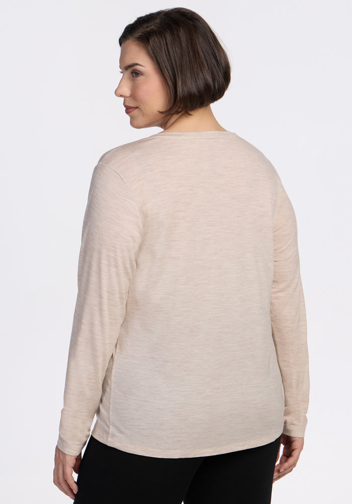 A woman with short brown hair stands facing away, wearing the Woolx Millie Long Sleeve in Cream Heather and black pants against a plain white background.