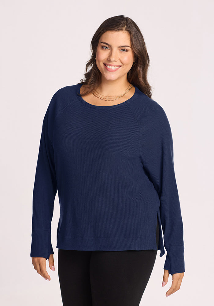 Woman smiling in the Woolx Ainsley Sweater - Ocean Cavern and black pants, standing against a light background. 
