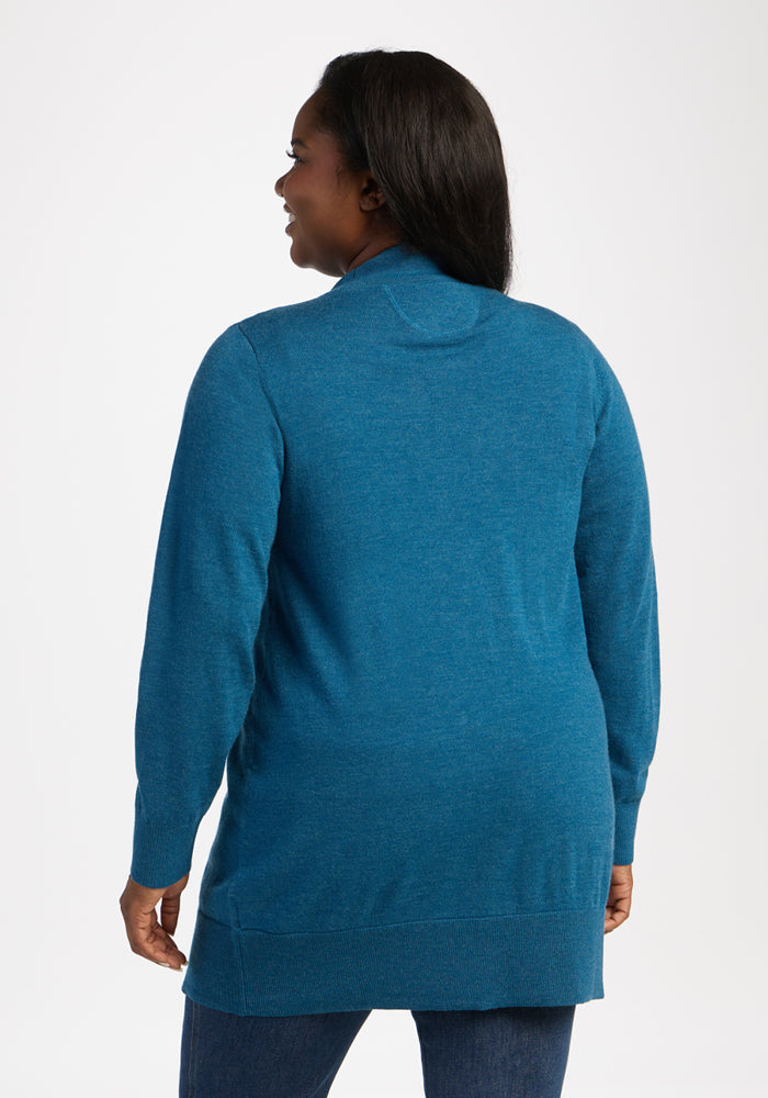 Woman in a Woolx Macie Sweater - Blue Pine and jeans, facing away, standing against a plain white background.