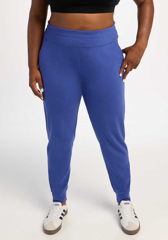 Person wearing Woolx Madden Joggers in royal blue, white Adidas sneakers, and a black crop top on a white background.