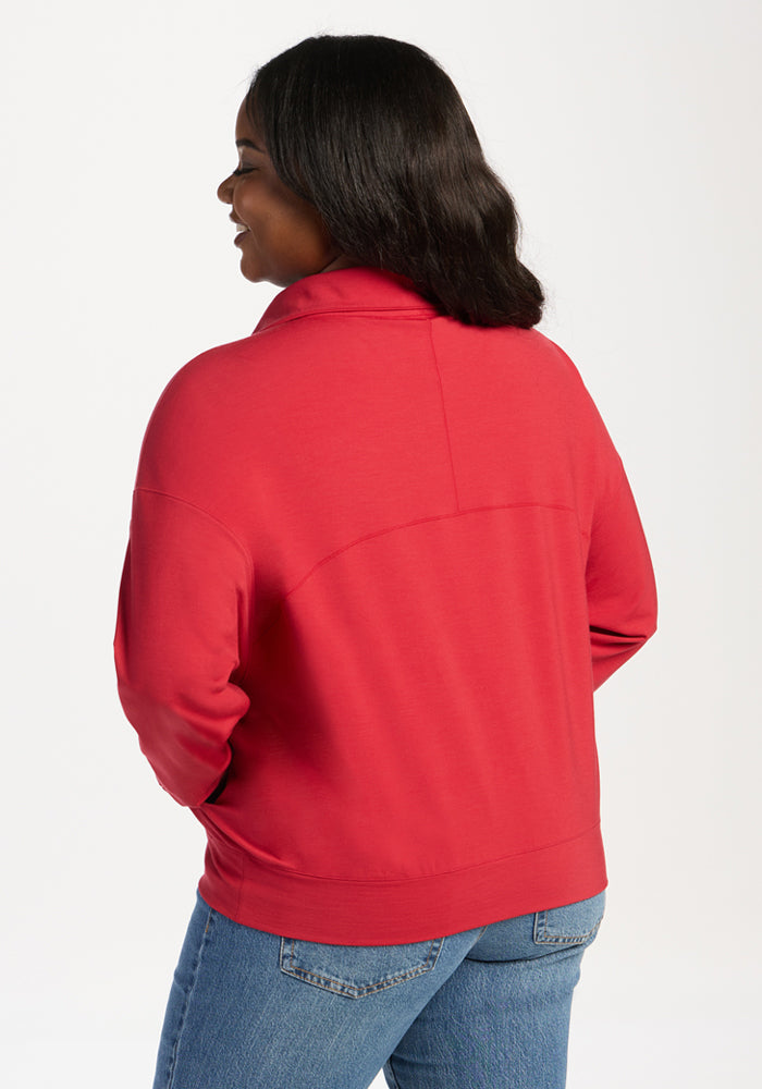 A woman seen from the back wearing a red Woolx Tori 1/4 Zip - Maraschino Cherry merino pullover and blue jeans.