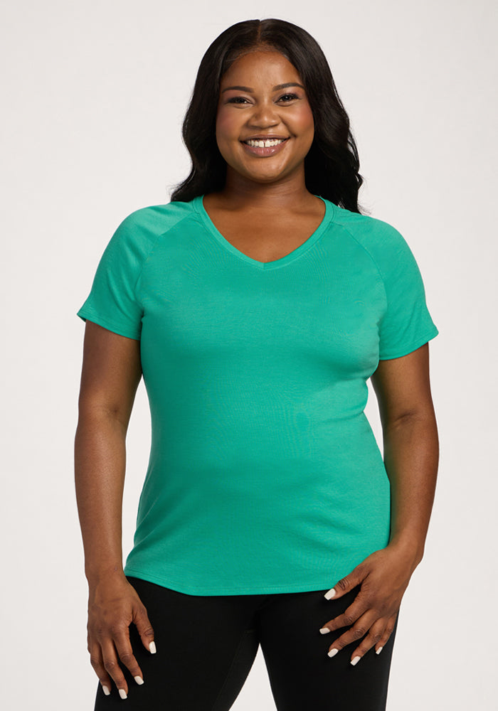 Smiling woman wears the Woolx Mia V Neck - Jungle with black pants, standing against a plain light background. 