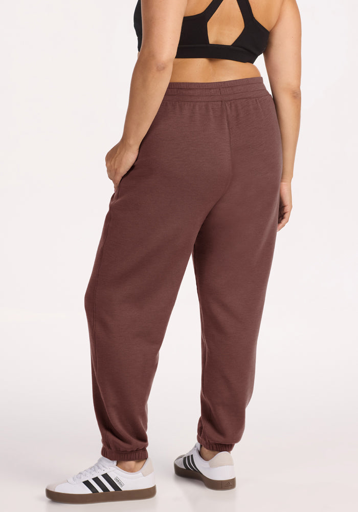 Person in Parker Sweatpants - Canyon Clay by Woolx, black sports bra, and white Adidas sneakers, standing away.