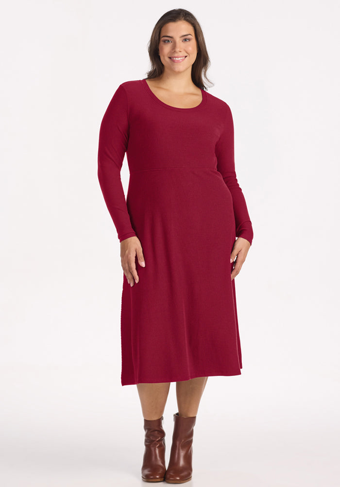 Woman in the Woolx Caroline Ribbed Twirl Dress in Beet Red and brown ankle boots, smiling against a plain background. 